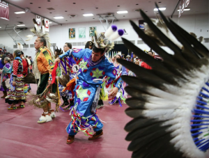  Native Americans dancing in traditional clothing in the Augsburg Gym